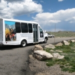 A white bus driving down a road with mountains in the background.