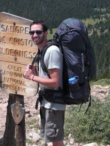 A man with a backpack standing next to a sign.