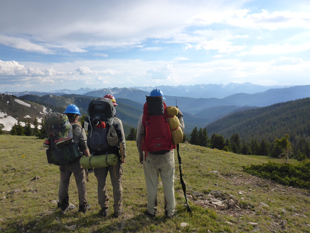 Three hikers with backpacks and helmets standing on a mountain