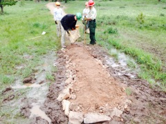 Two park rangers examining a recently uncovered dinosaur fossil in a muddy excavation site.