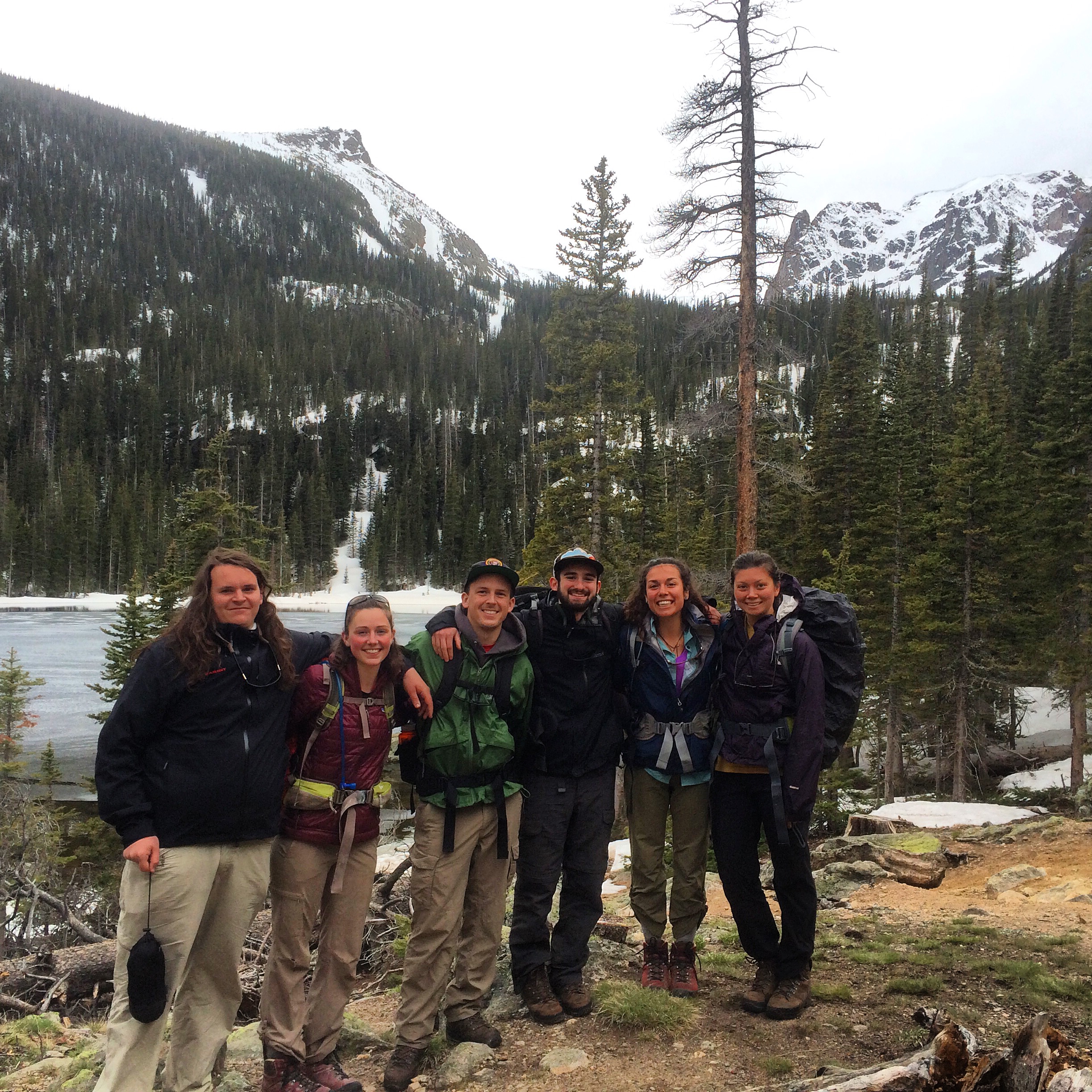 Group of six hikers smiling in front of a snowy mountain landscape