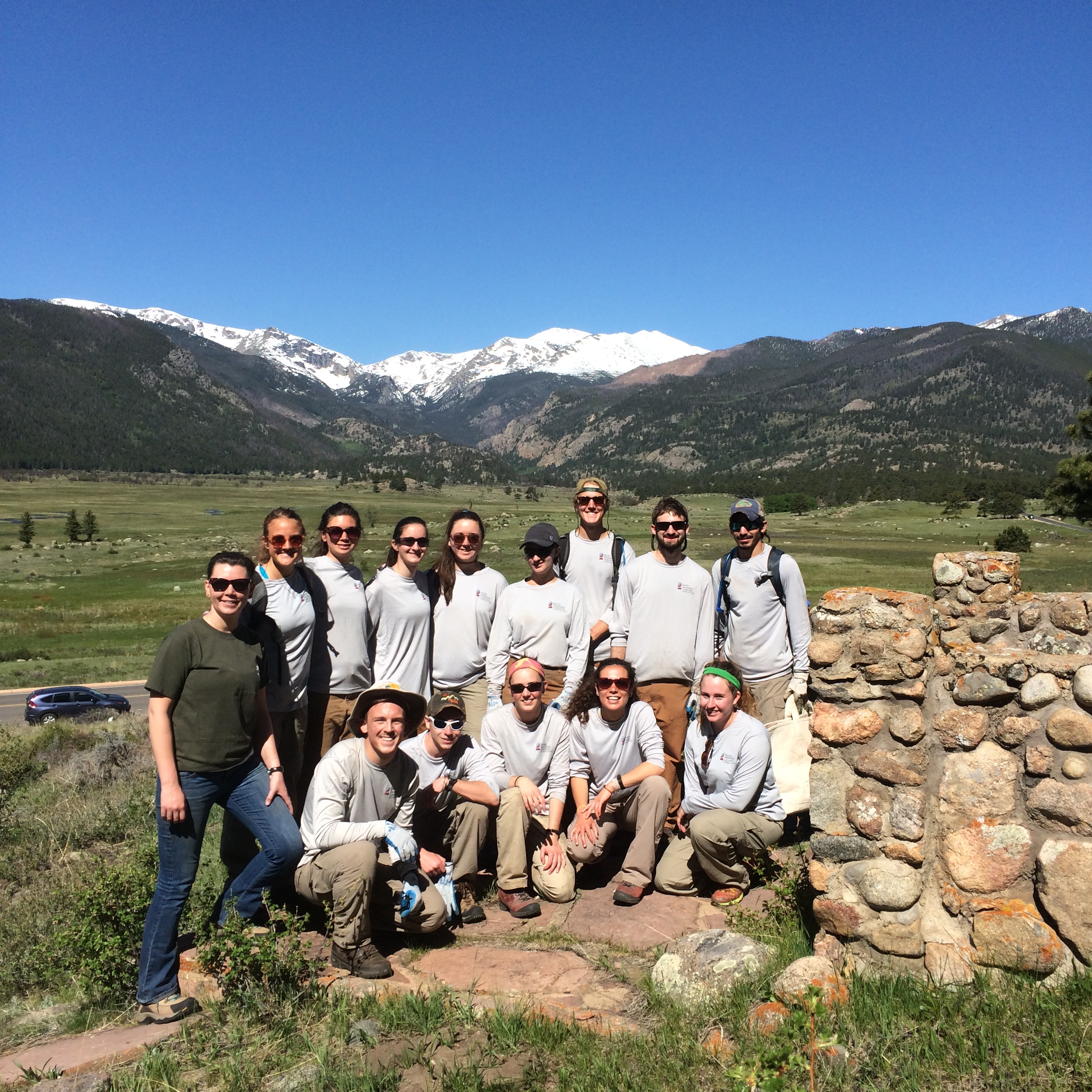 Group of people posing in front of a scenic mountain landscape on a sunny day.