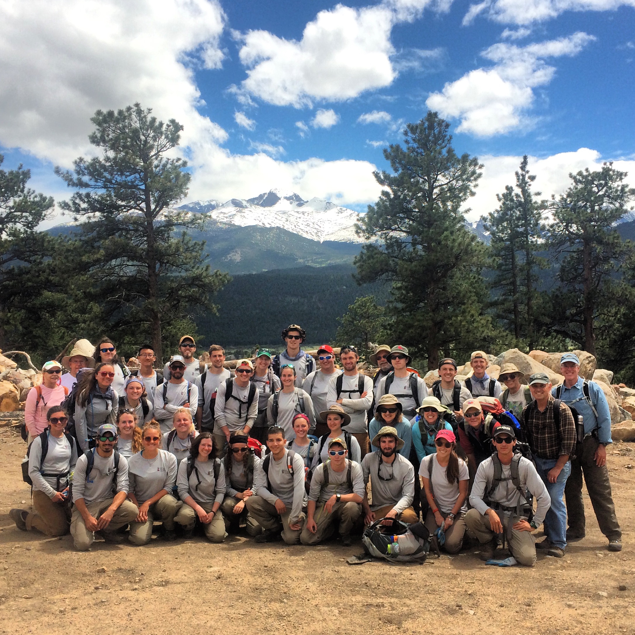 A large group of hikers posing in front of snowy mountain peaks
