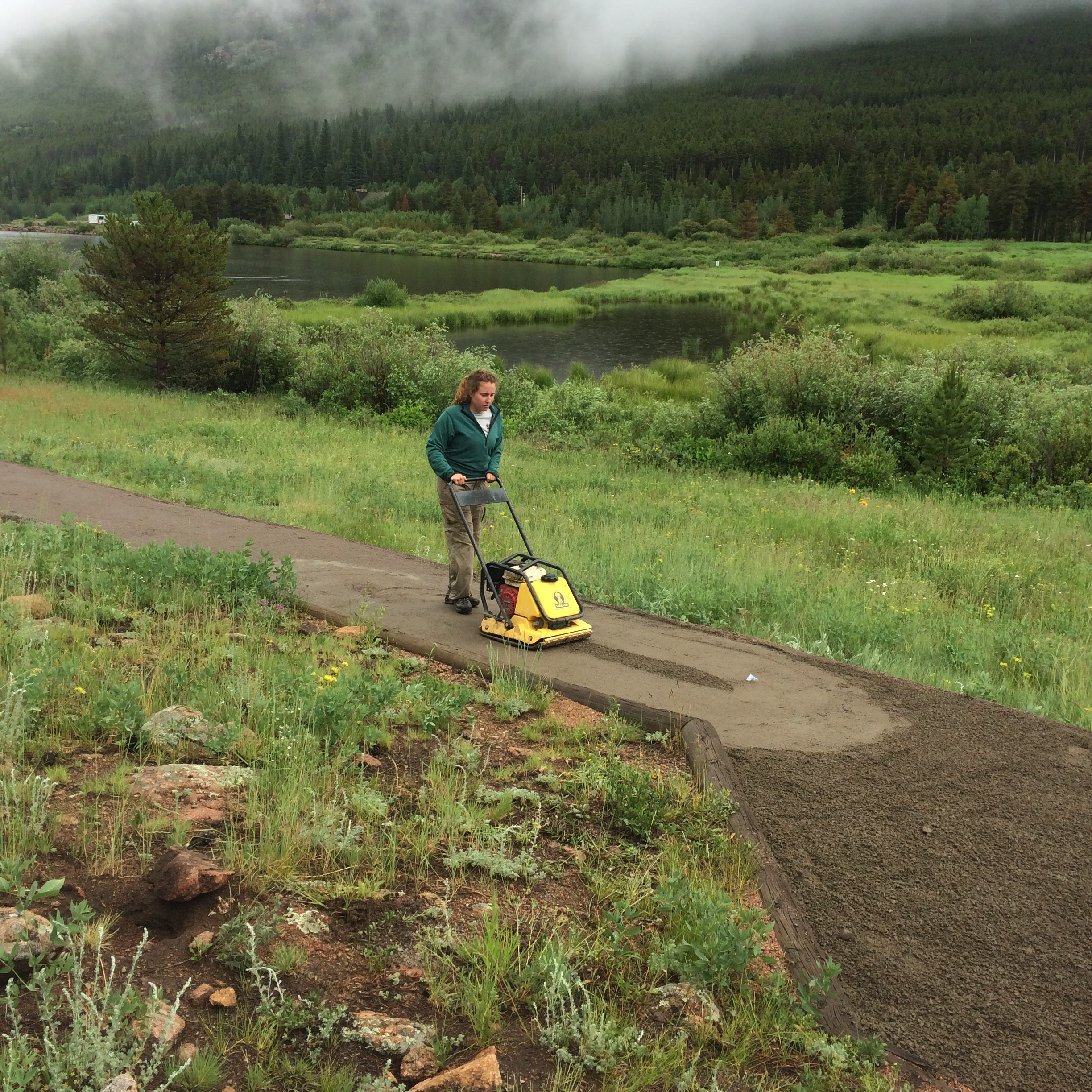 A person using a compact yellow plate compactor on a dirt path