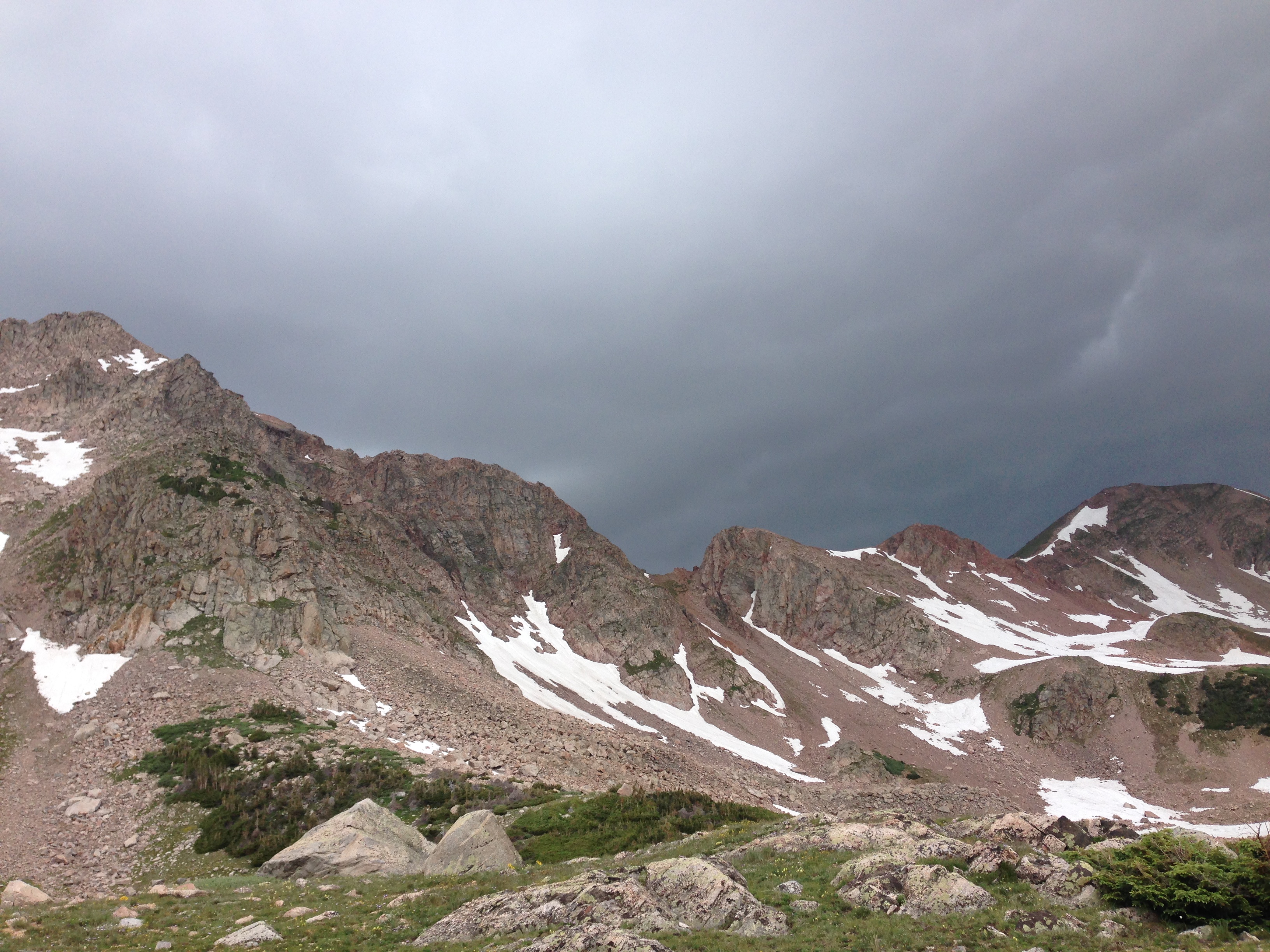 Stormy sky over a rugged mountain landscape with patches of snow.