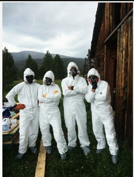 Four people in white hazmat suits standing against a wooden building