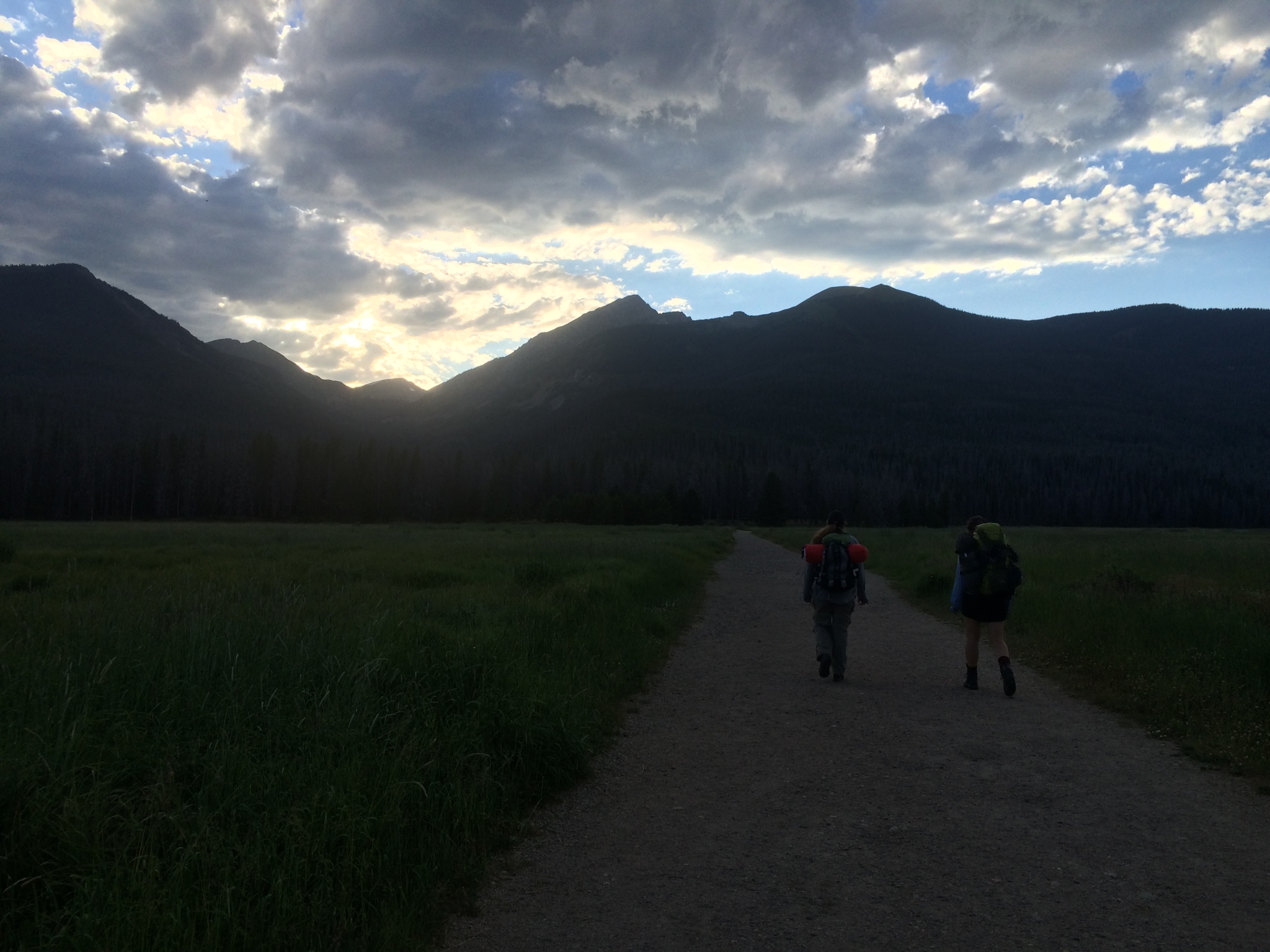Two hikers with backpacks walking on a trail through a grassy valley