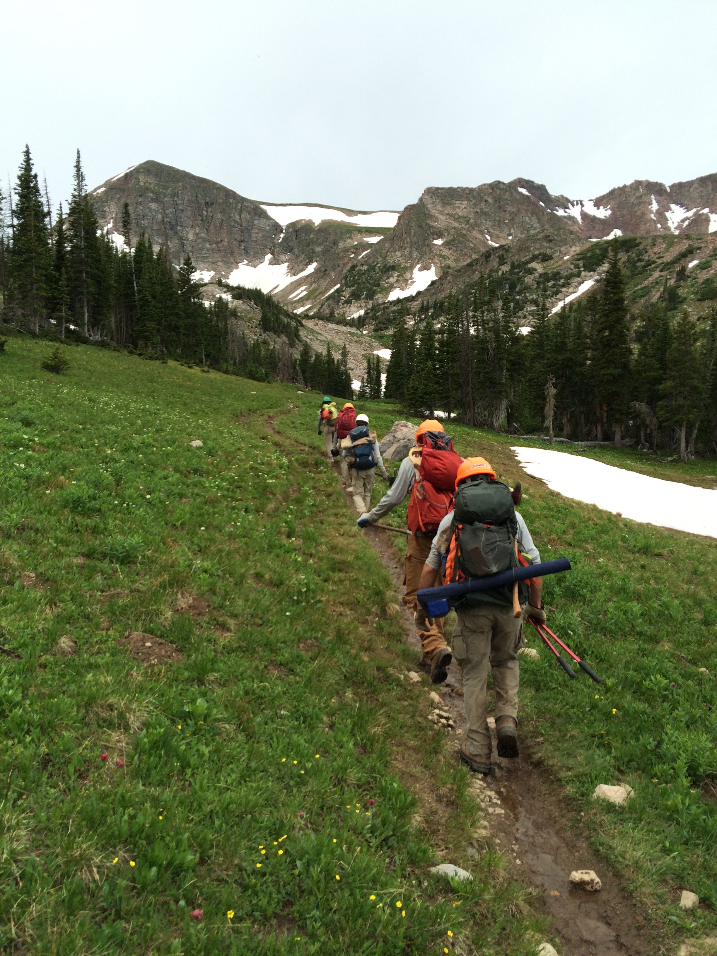 Hikers with backpacks trekking along a narrow trail in a mountainous landscape