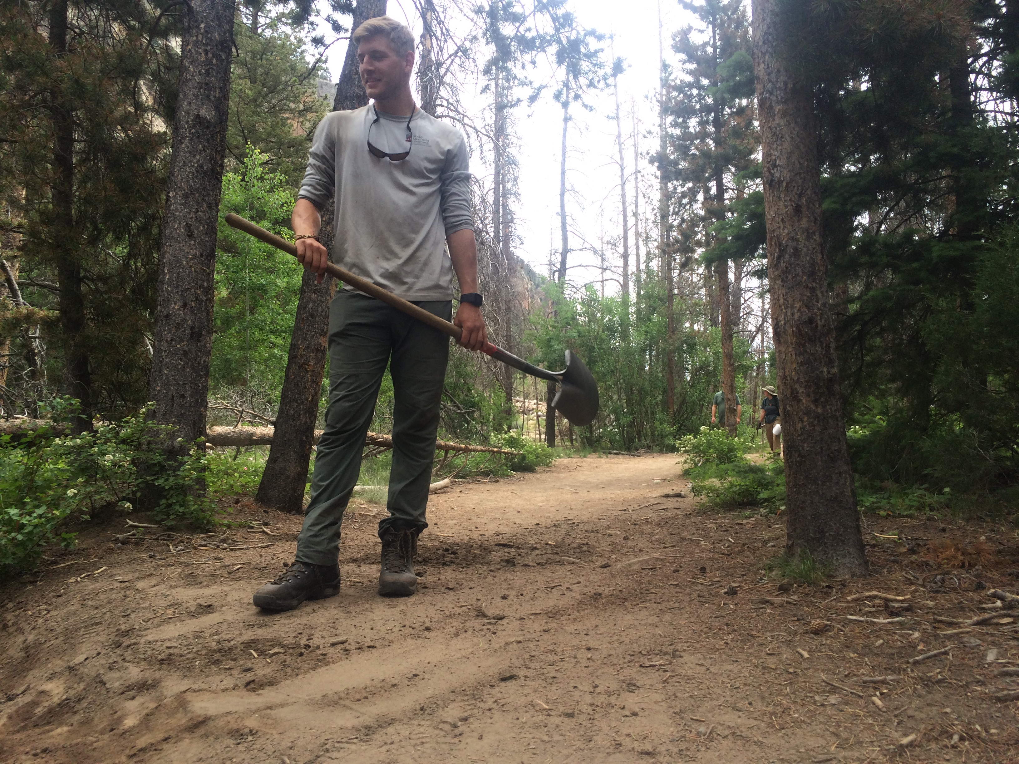 A man stands on a forest trail holding a shovel
