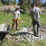 Two men working on a pile of rocks in a field.