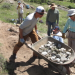 A group of people working on a trail with a wheelbarrow.