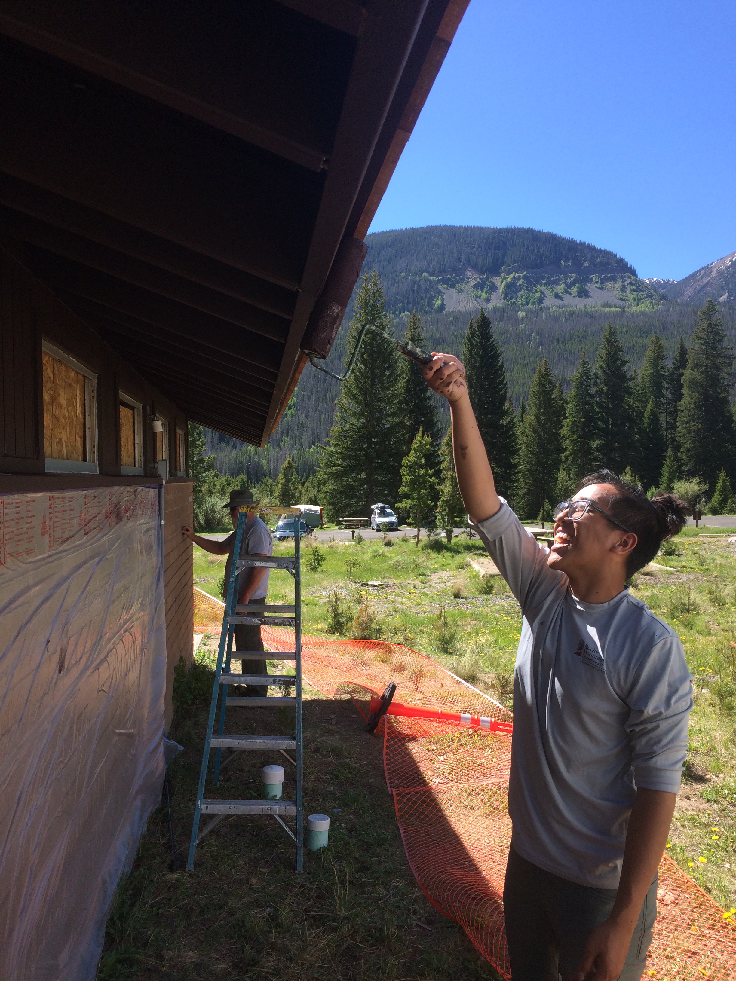 Workers painting a comfort station situated on a grassy field