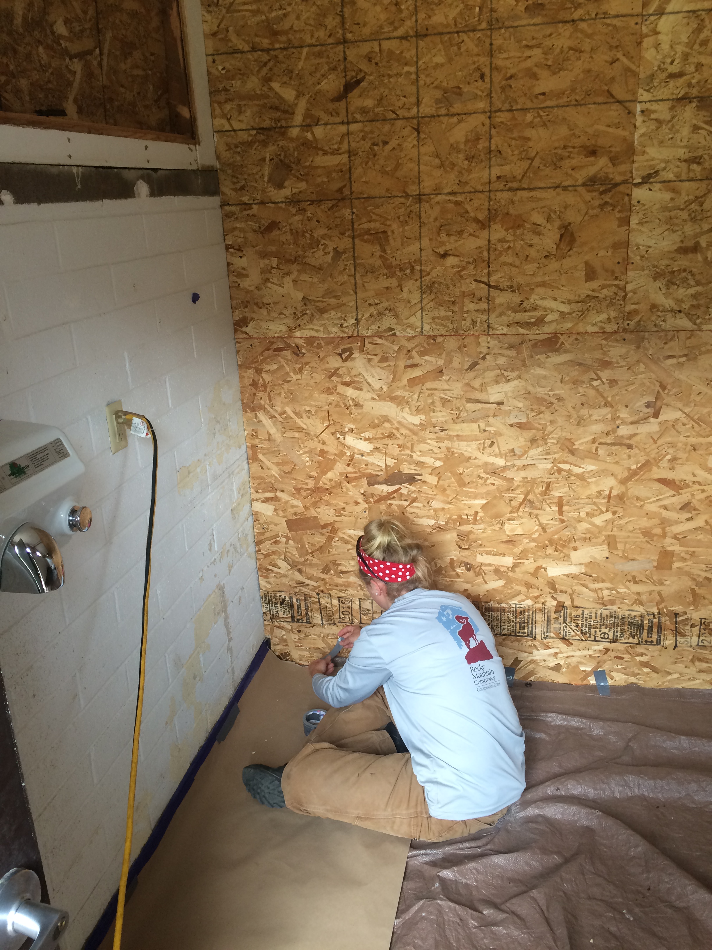 A worker sitting and applying glue or sealant to particle board wall panels