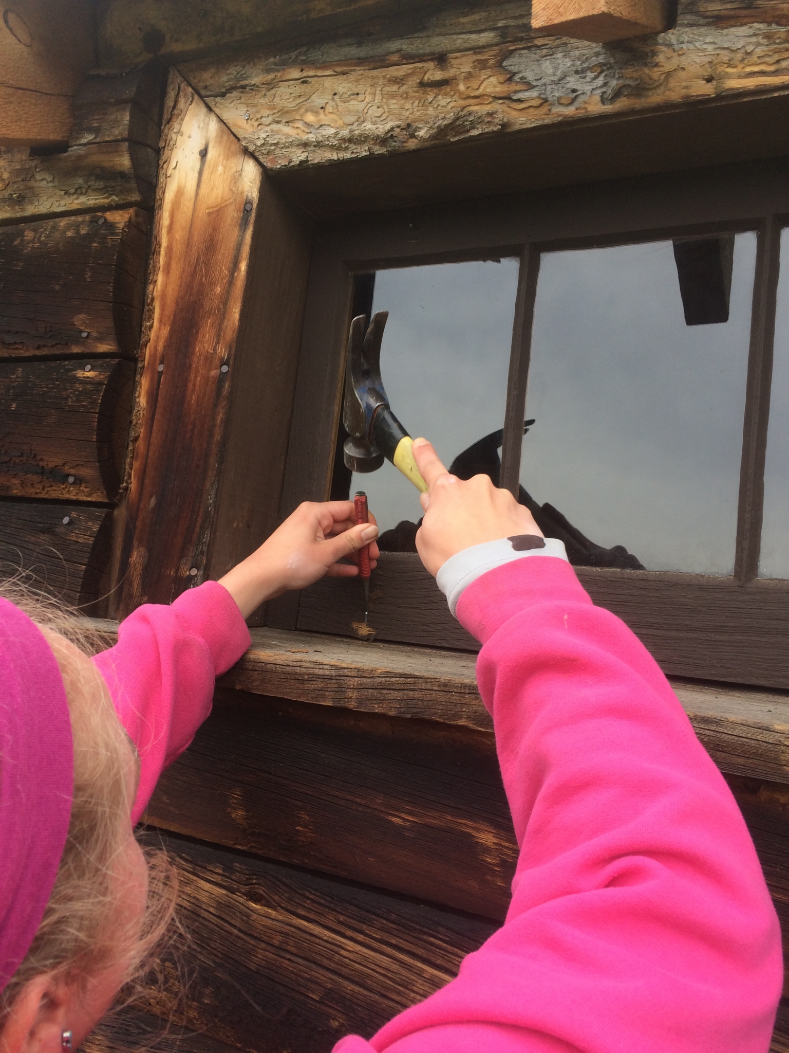 A person in a pink sleeve using a caulking gun to apply sealant around a wooden window frame.