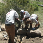 A group of men working on a rock in the woods.