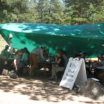 A group of people sitting under a green tarp.
