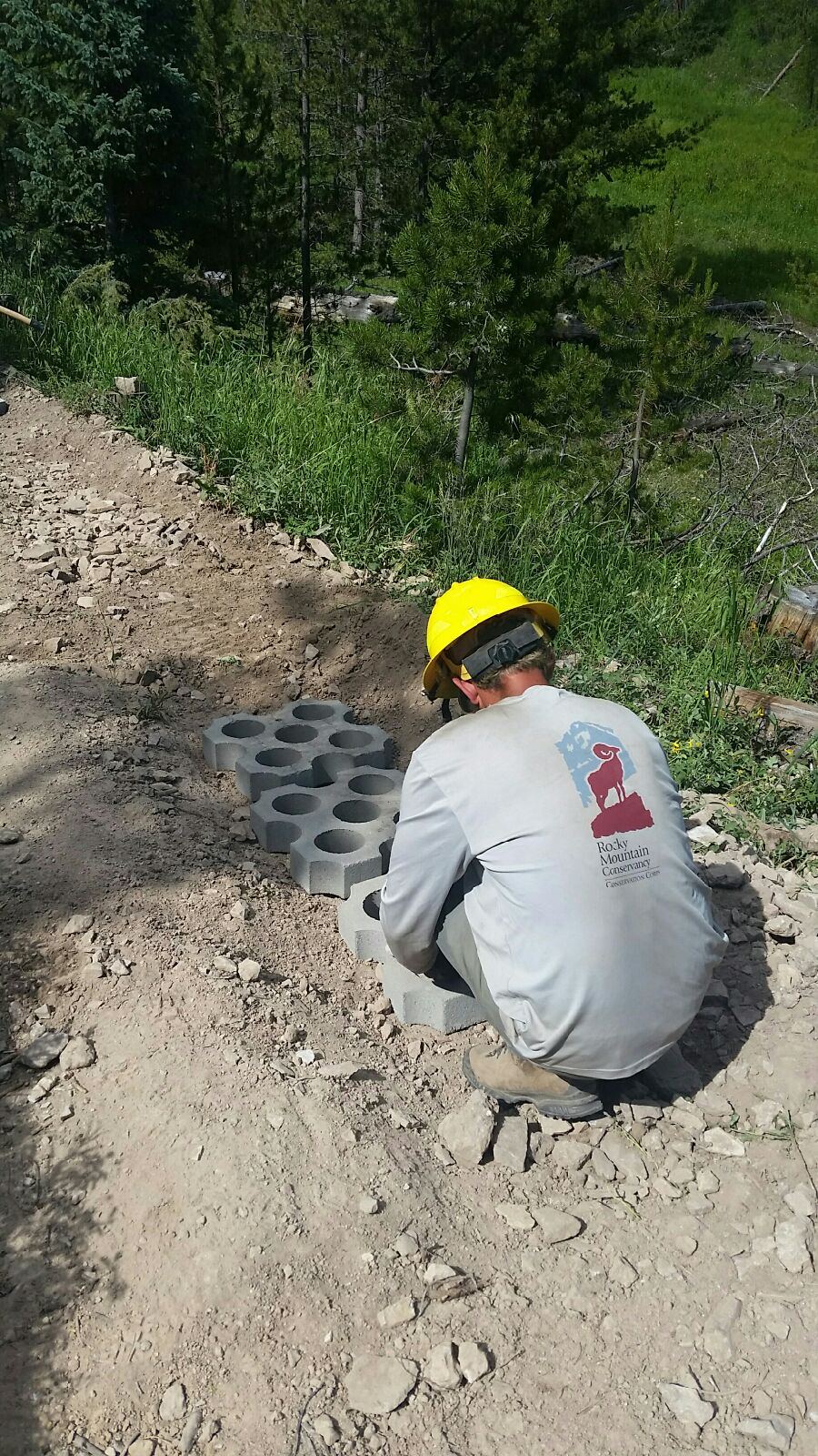 A worker in a yellow helmet installs hexagonal paving blocks on a trail