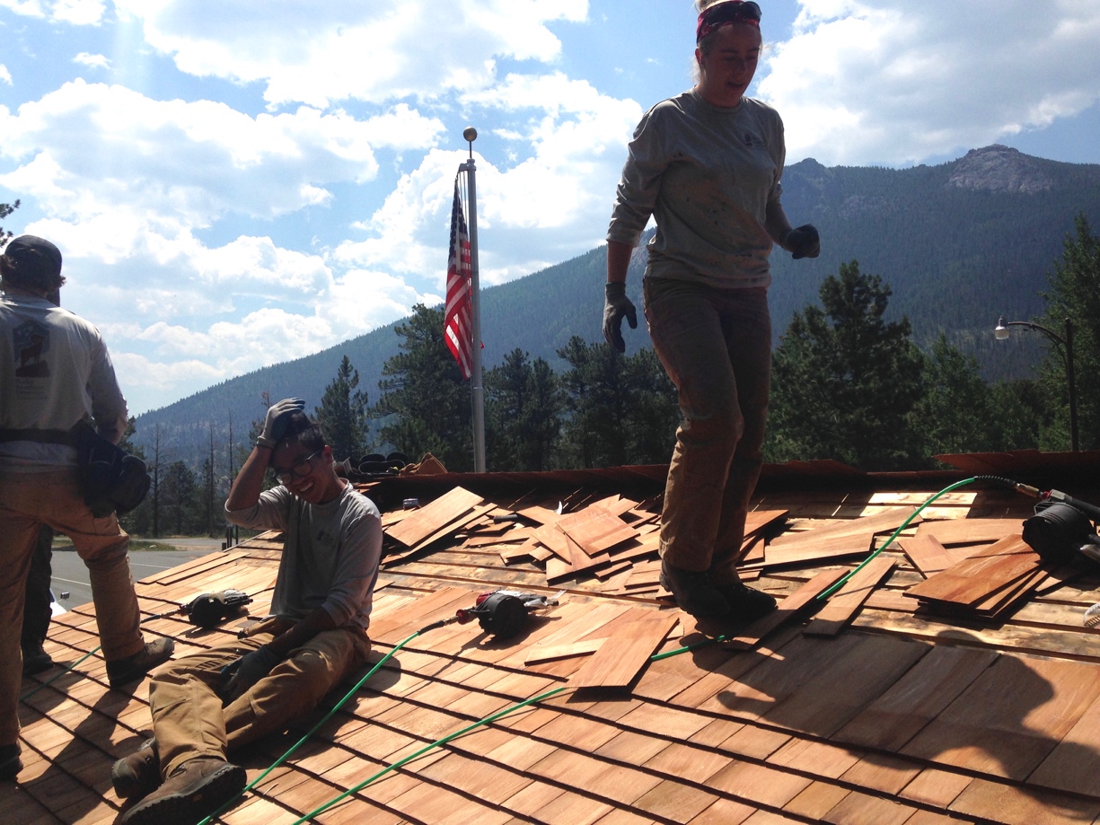 Four workers replacing shingles on a roof with tools scattered around