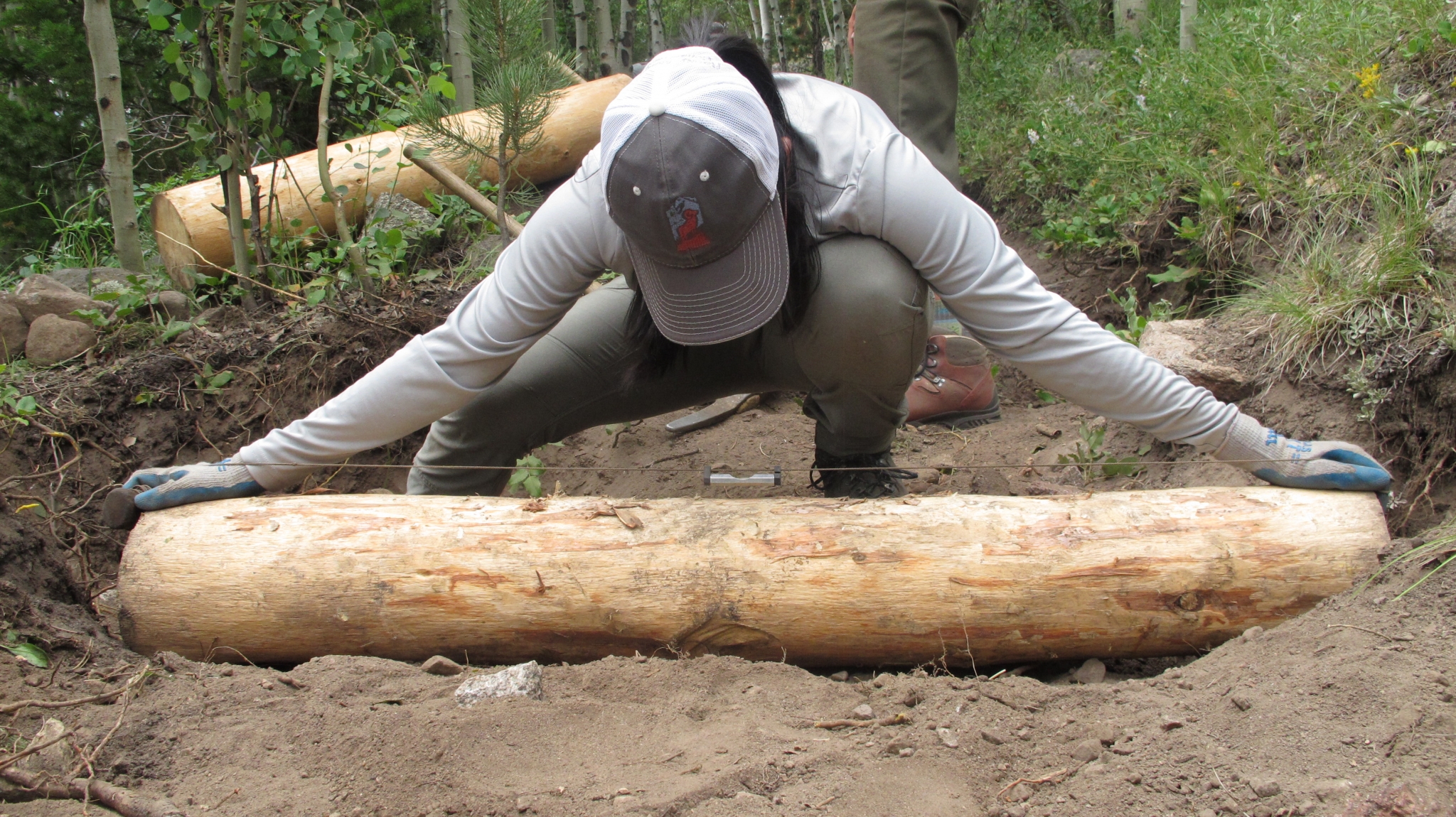 A person in work clothes and gloves dragging a short log