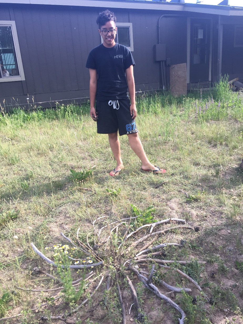 A young man standing in a grassy field in front of a cabin