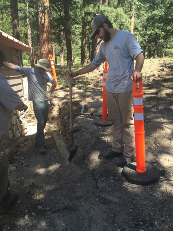 Two forest rangers in a wooded area, with orange traffic cones nearby.