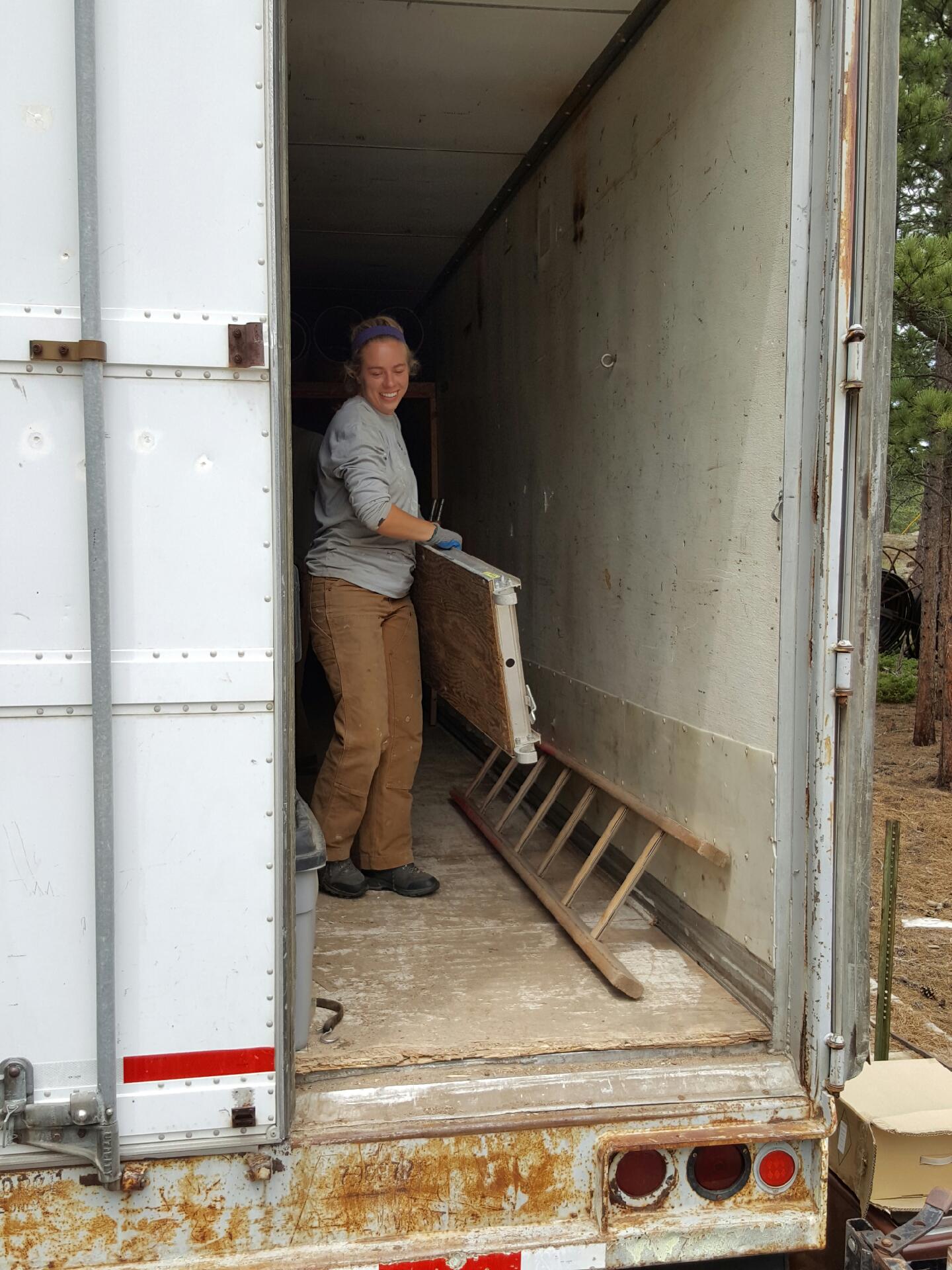 A woman smiling and standing inside an open, empty cargo truck, holding a door