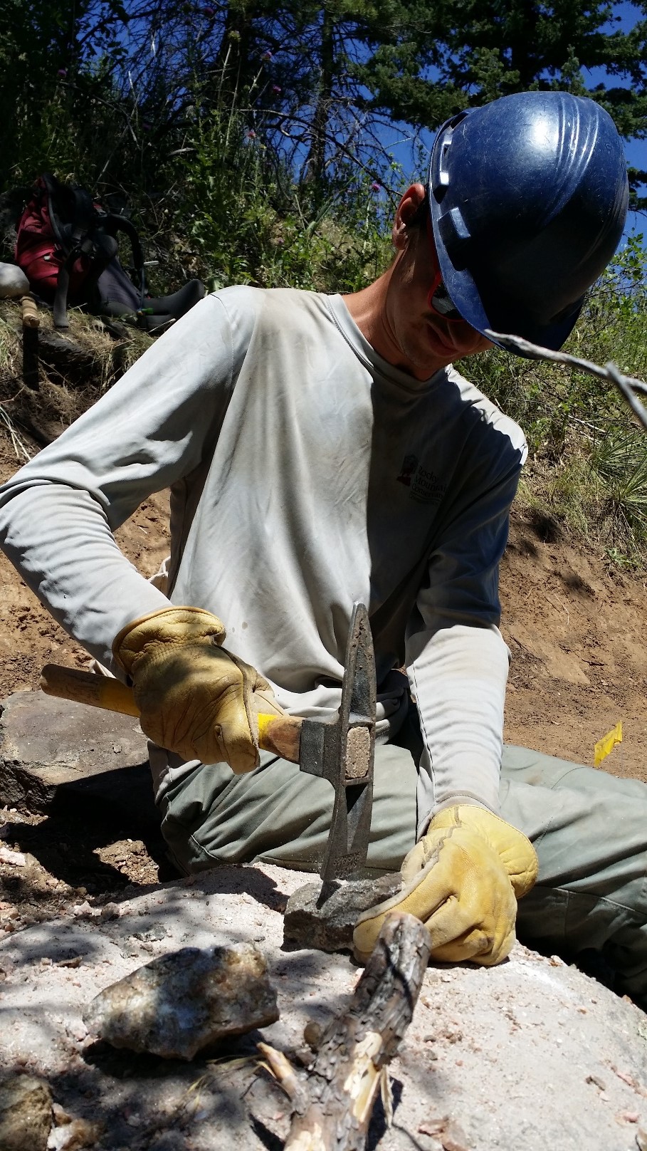 Man using a hammer and chisel on a rock outdoors