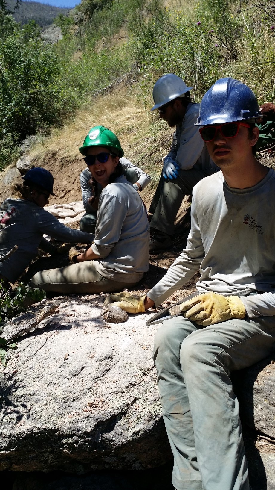 Five workers in helmets and gloves taking a break on a rocky terrain