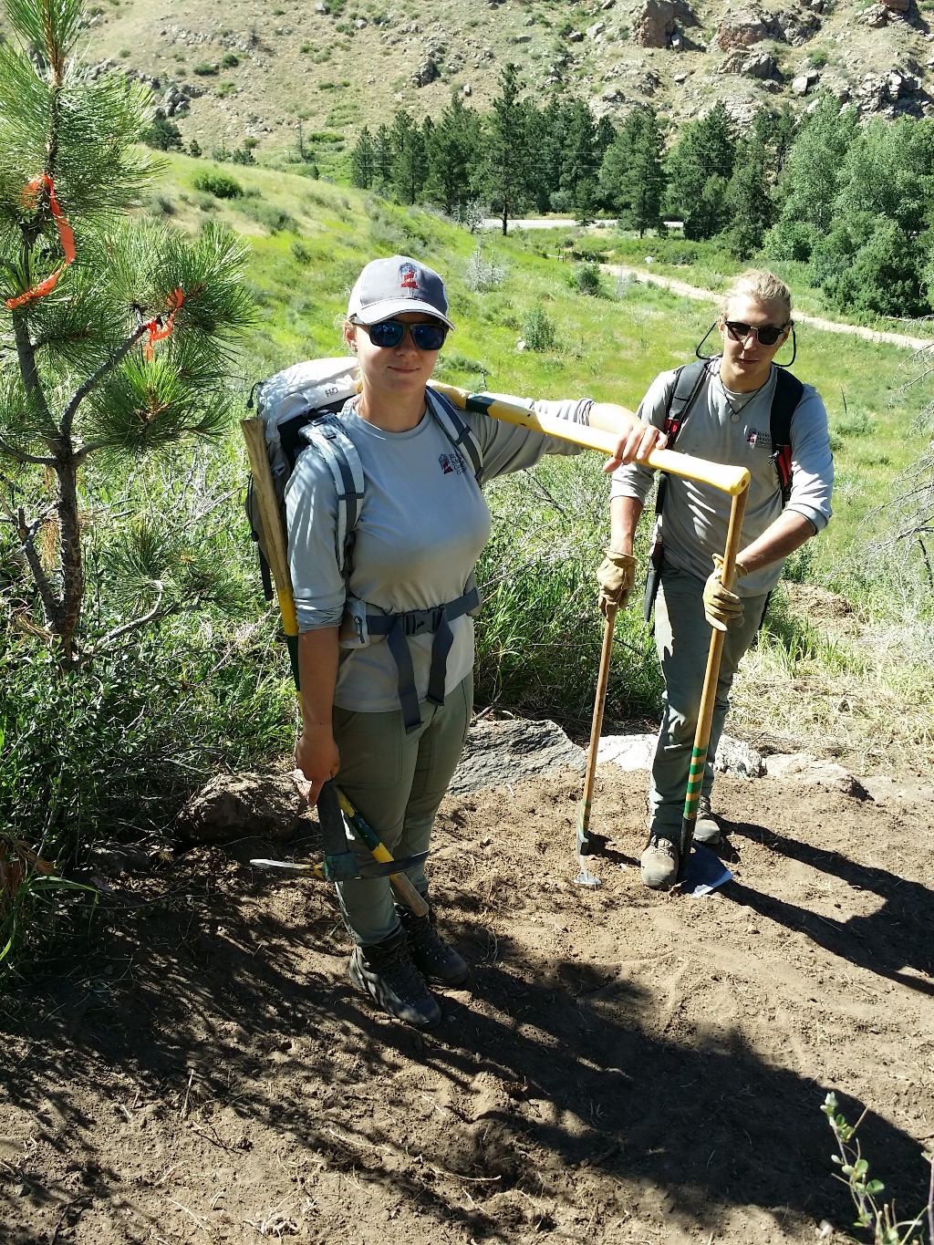 Two hikers with backpacks and walking sticks standing on a mountain trail