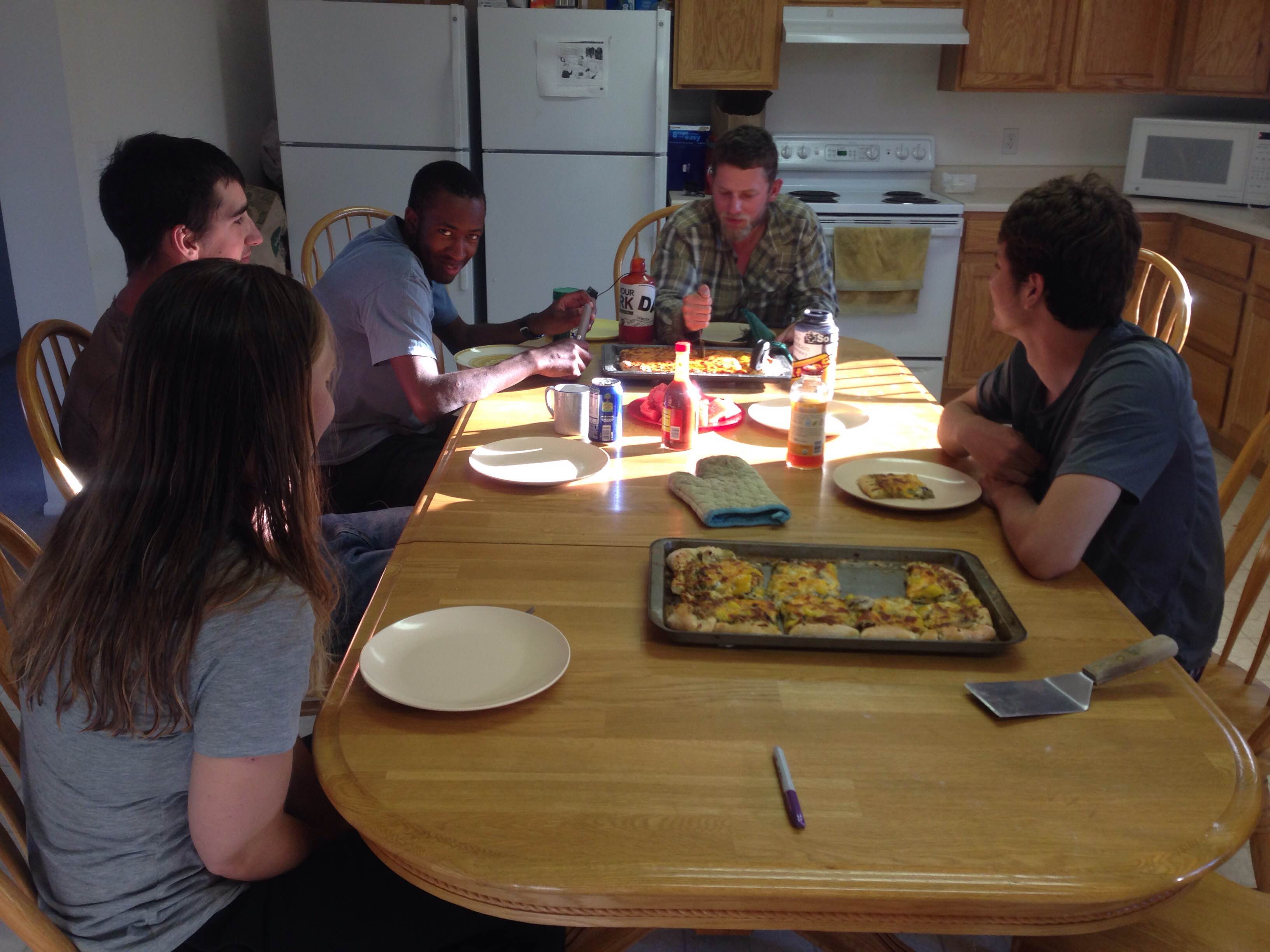 Group of six people enjoying a meal together around a dining table in a bright kitchen.