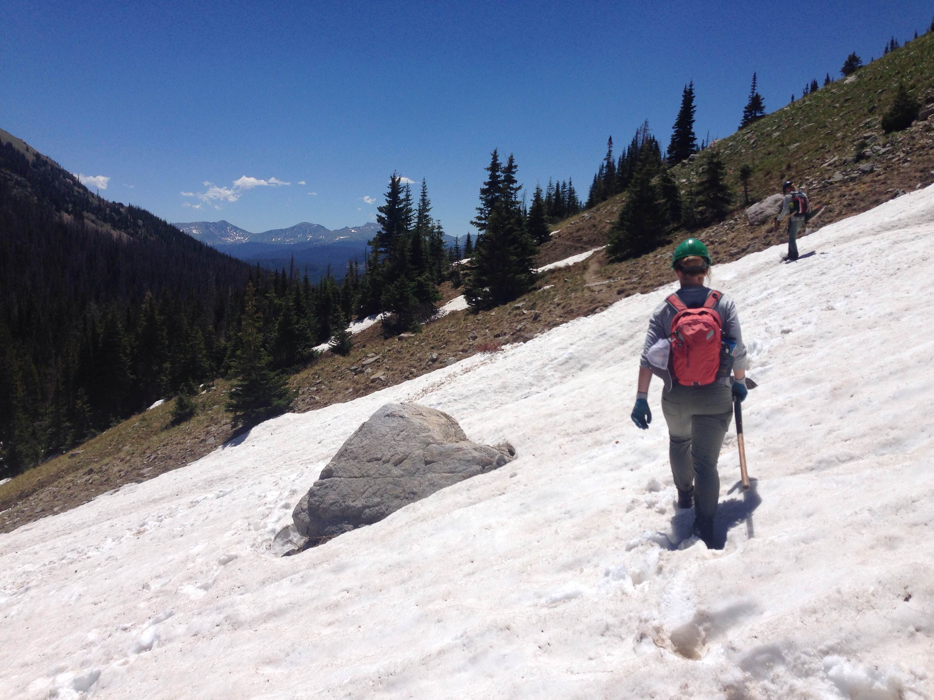 A hiker walking on a snowy trail in the mountains on a sunny day.