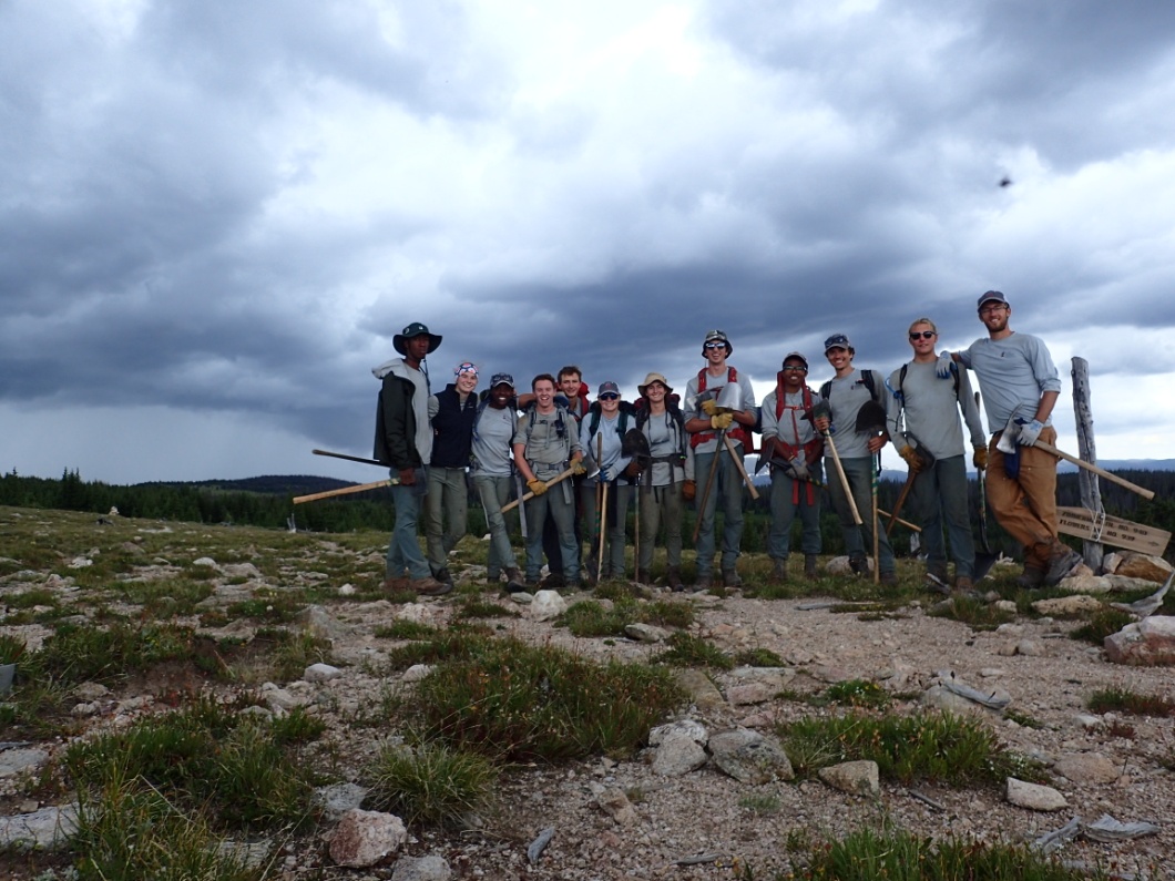 Group of volunteers posing with tools on a rocky terrain under cloudy skies
