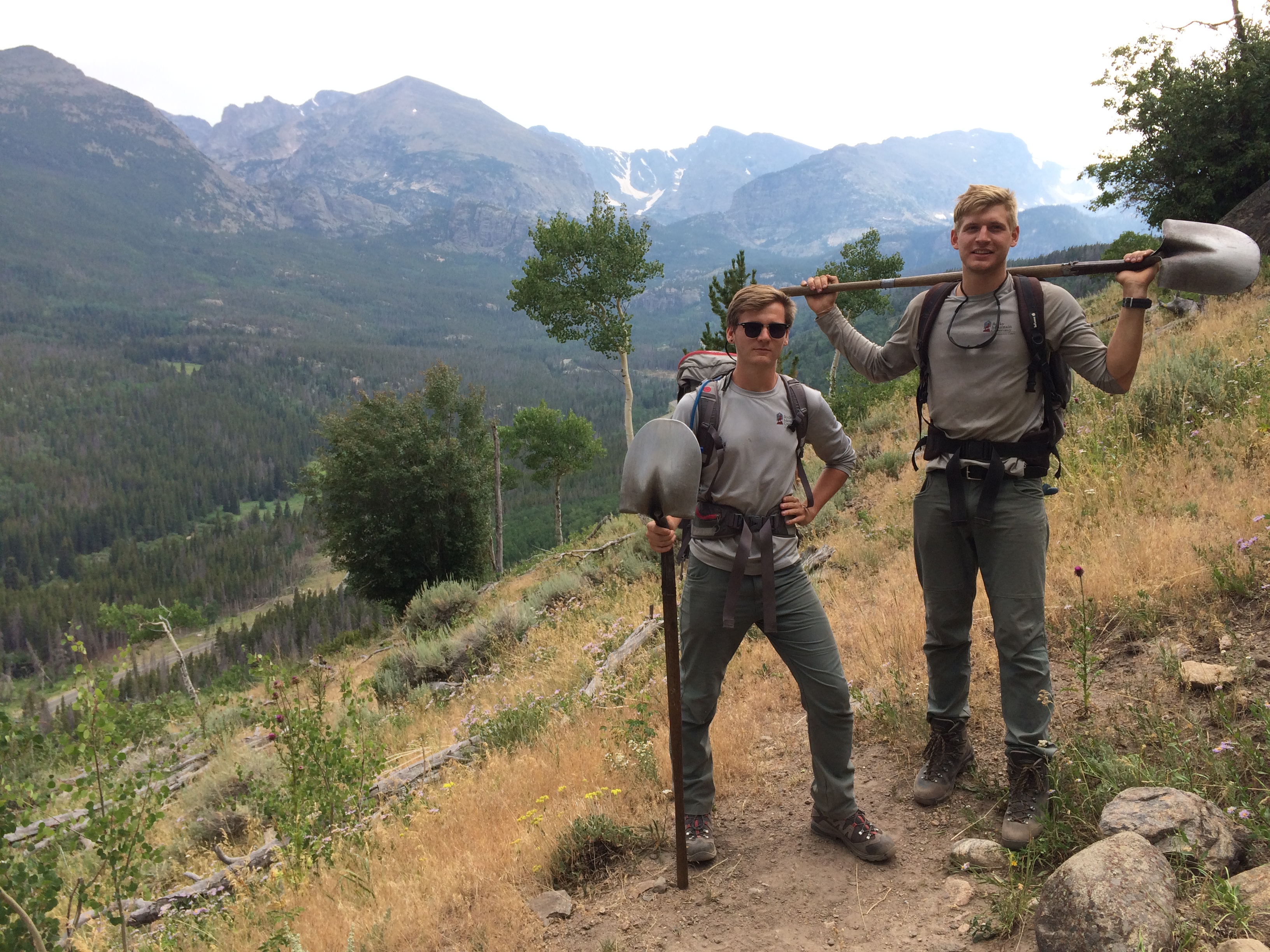 Two hikers holding paddles on a trail with mountain views in the background.