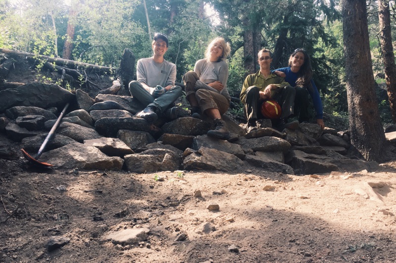 Four friends sitting on a rocky wall in a forest