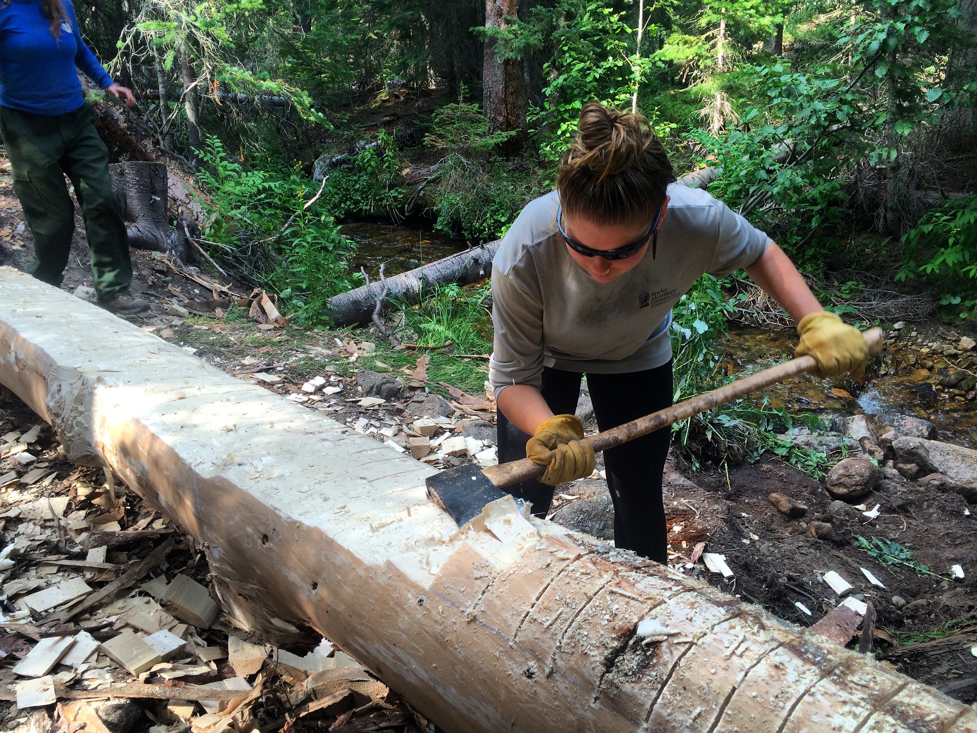 A person using an axe to peel bark off a log in a wooded area