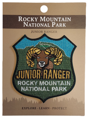 Junior Ranger patch featuring a ram design for Rocky Mountain National Park, presented on a brown card with "Explore • Learn • Protect.