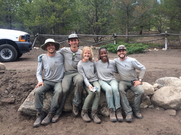 Five conservation workers in matching uniforms sitting on a log