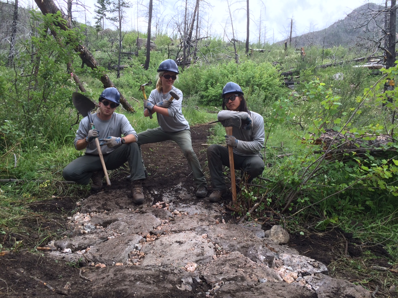 Three forest workers posing with shovels on a muddy trail