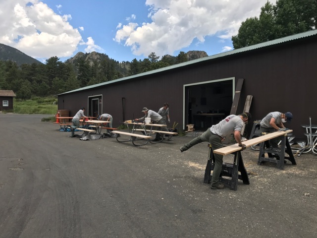 Men in gray uniforms building wooden furniture outdoors