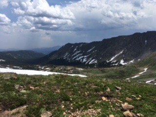 Mountain landscape with patches of snow, under a cloudy sky.