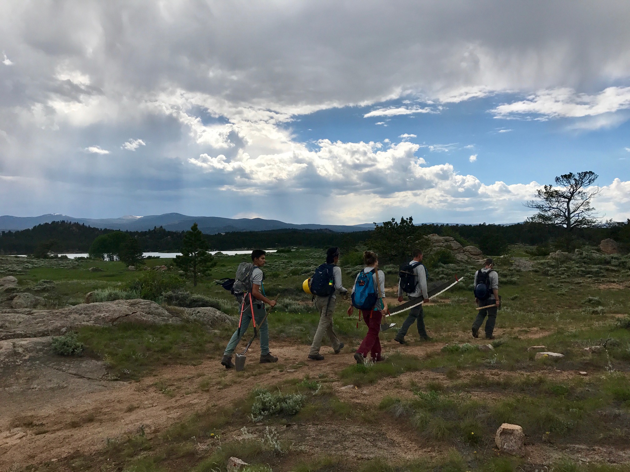 A group of five hikers carrying tools walks through a rocky terrain