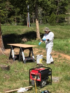 Person in a protective suit spray painting a wooden board on a table outdoors