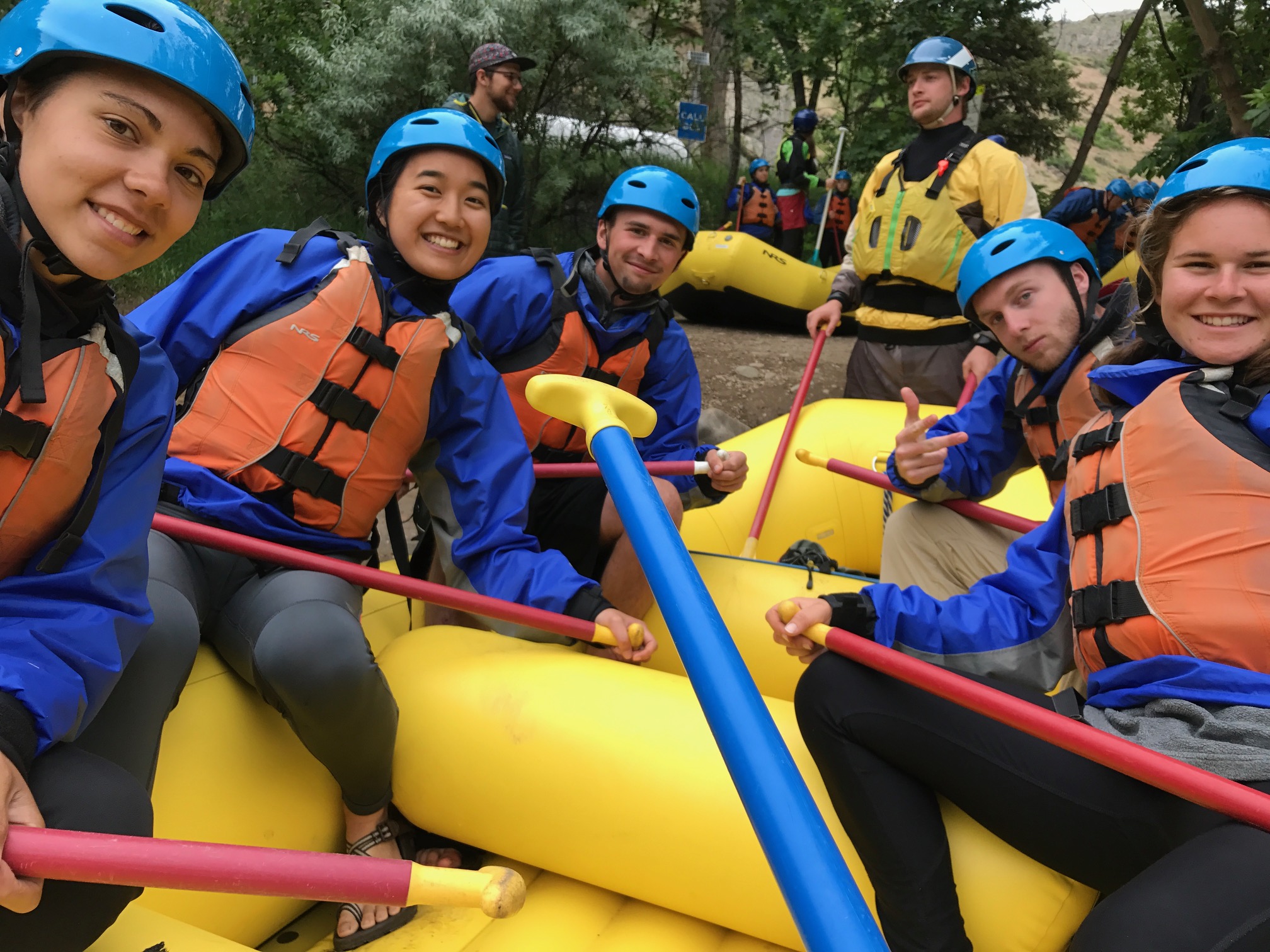 Group of five people in helmets and life vests holding paddles on a yellow raft
