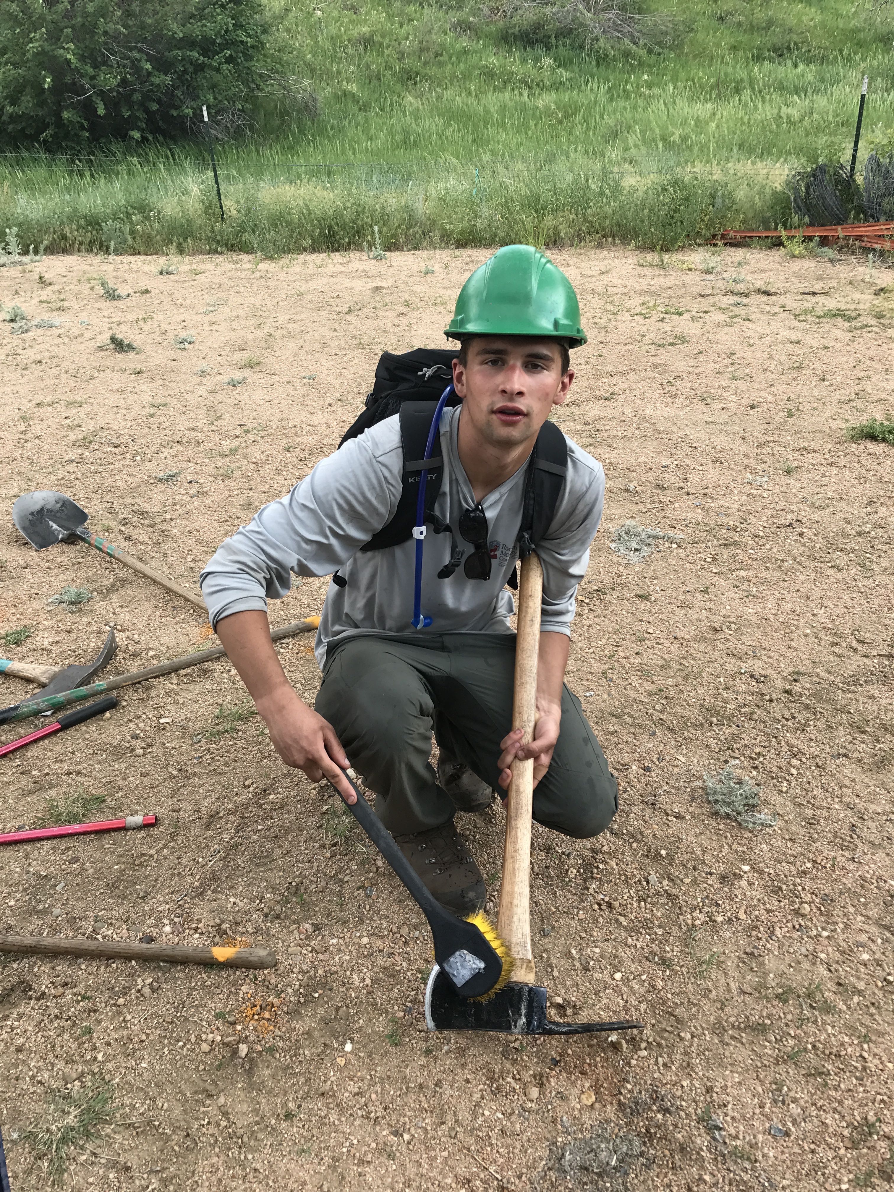 A young man wearing a green helmet and a backpack kneels
