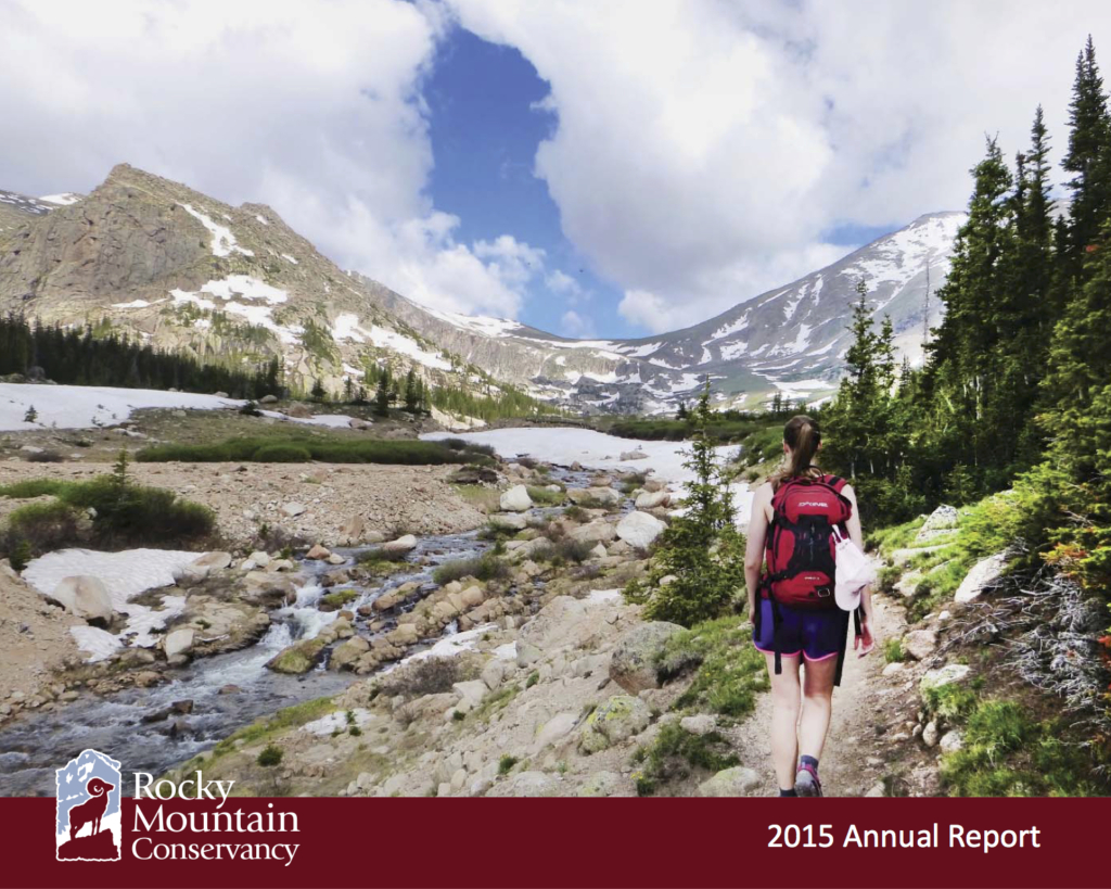 A woman is walking down a trail with mountains in the background.