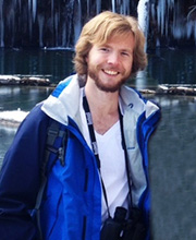 A man in a blue jacket standing in front of a waterfall.