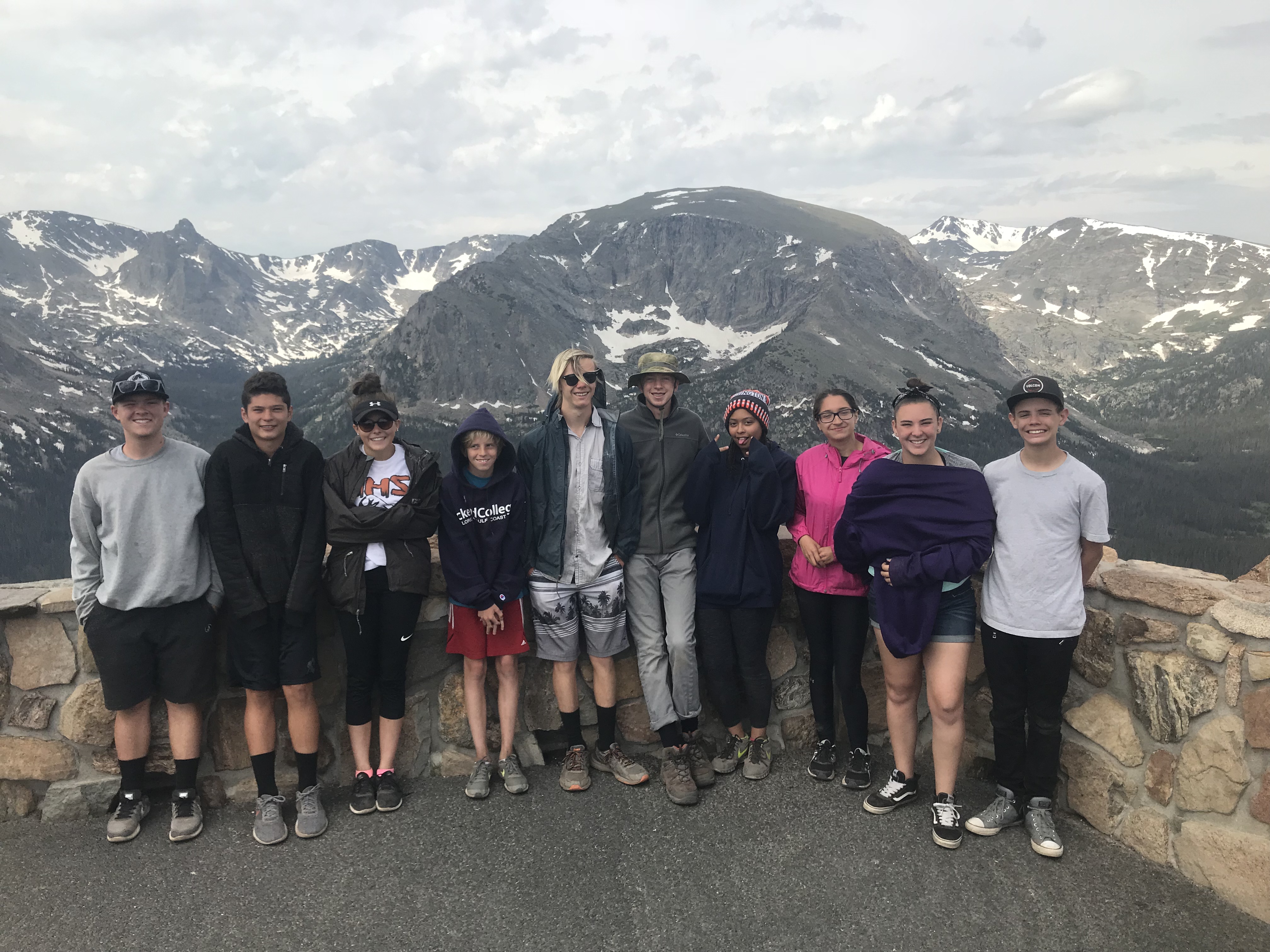 Group of ten people posing together in front of a mountainous landscape at a scenic overlook.