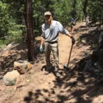 A man standing on a trail with a shovel.