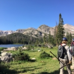 Two hikers walking down a trail near a lake.