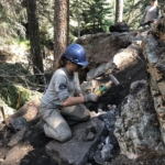 Two women working on a rock in the woods.